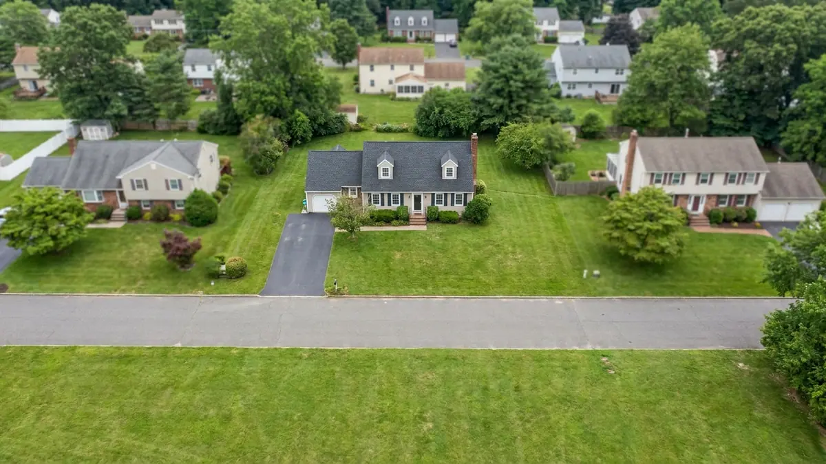 Overhead view of a two-story house with a gable asphalt shingle roof, two dormers and a brick chimney, driveway and lawn below