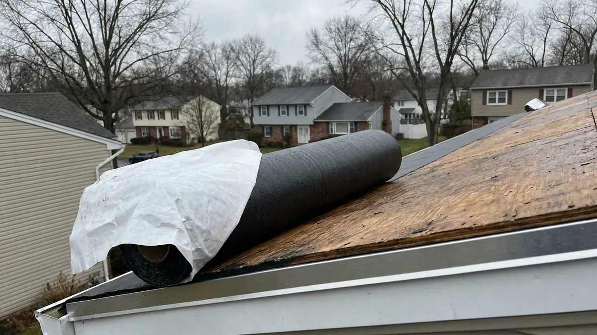 Self-adhered rubberized underlayment rolled along the eave of an exposed plywood roof deck with the release liner partly peeled back and aluminum drip edge at the fascia