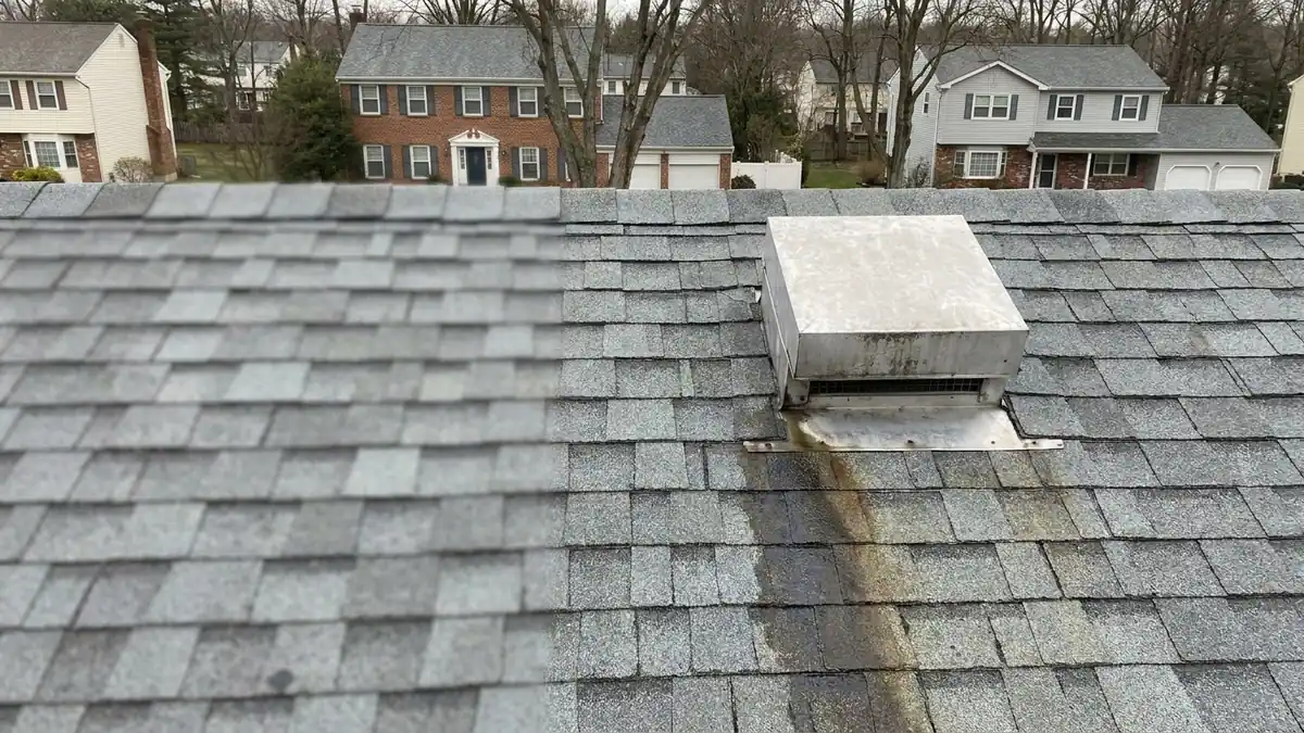 Close-up of a square aluminum box vent set into gray architectural shingles on a rain-dampened roof, with a dark water stain spreading on the shingles below its flashing