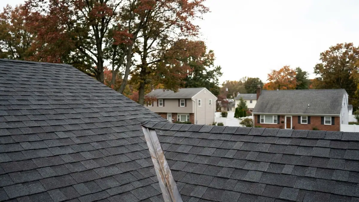 Roof valley where two shingled slopes meet, metal valley liner visible beneath charcoal architectural shingles under an overcast sky