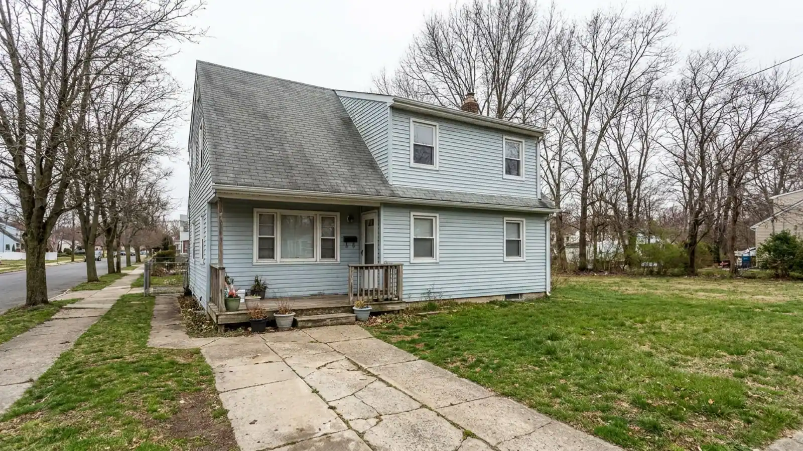 Two-story home with an aging gray asphalt shingle roof above faded light-blue vinyl siding, front walkway and small covered porch in soft daylight