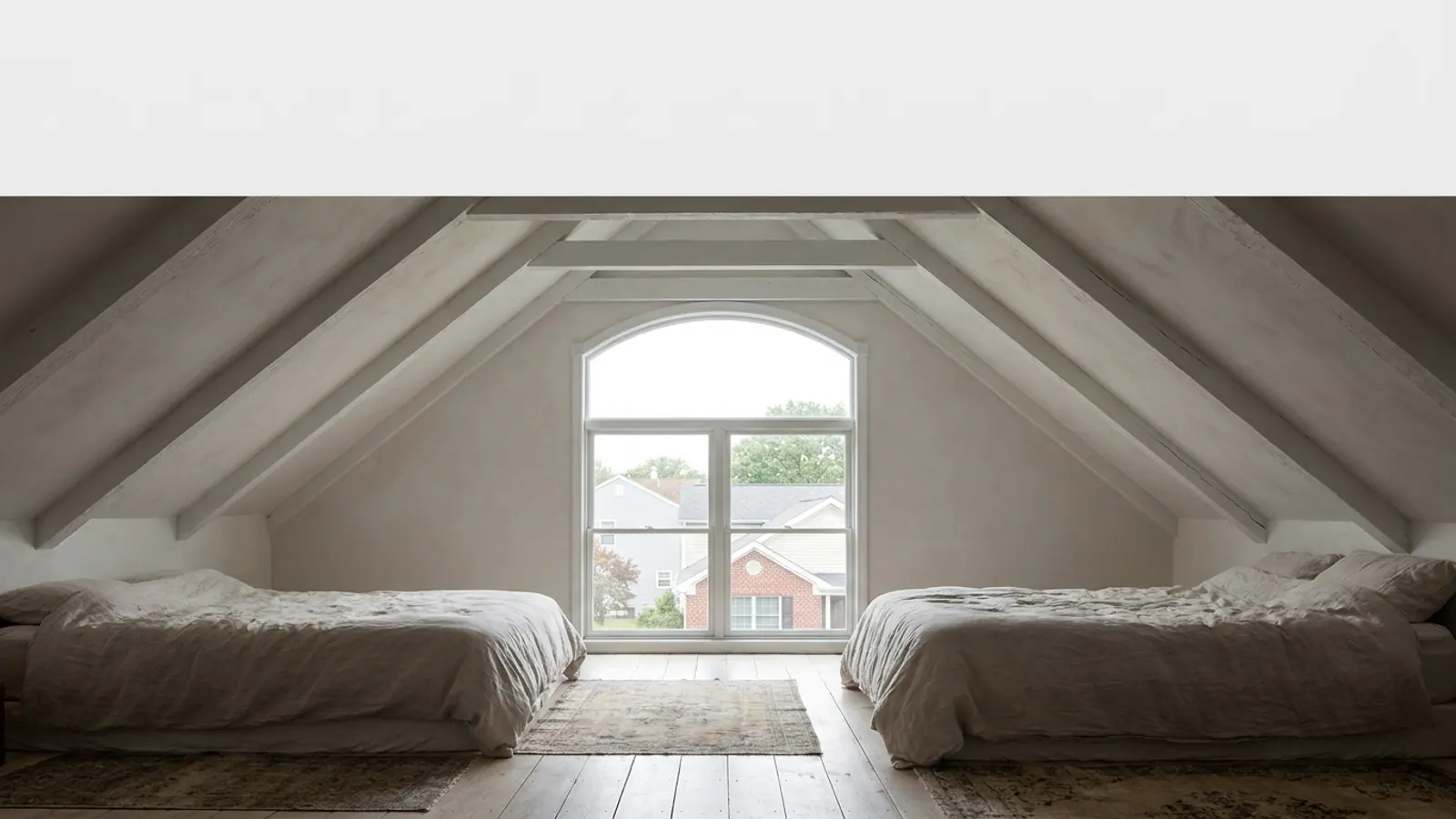 Bright bedroom with a sloped plaster cathedral ceiling, white-painted exposed beams and daylight coming in through a gable window