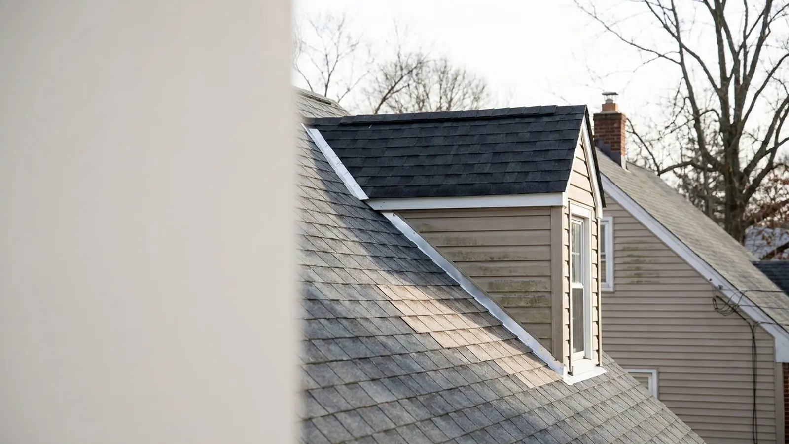 Close exterior view of a new shed dormer roof meeting an older main roof slope, with step flashing and fresh shingles along the joint in morning light