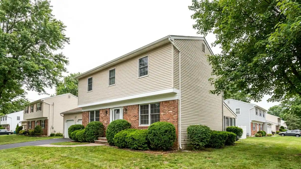 Two-story colonial with red brick across the lower front wall and light vinyl siding on the upper story and side wall, a trim line at the transition and clipped shrubs along the foundation